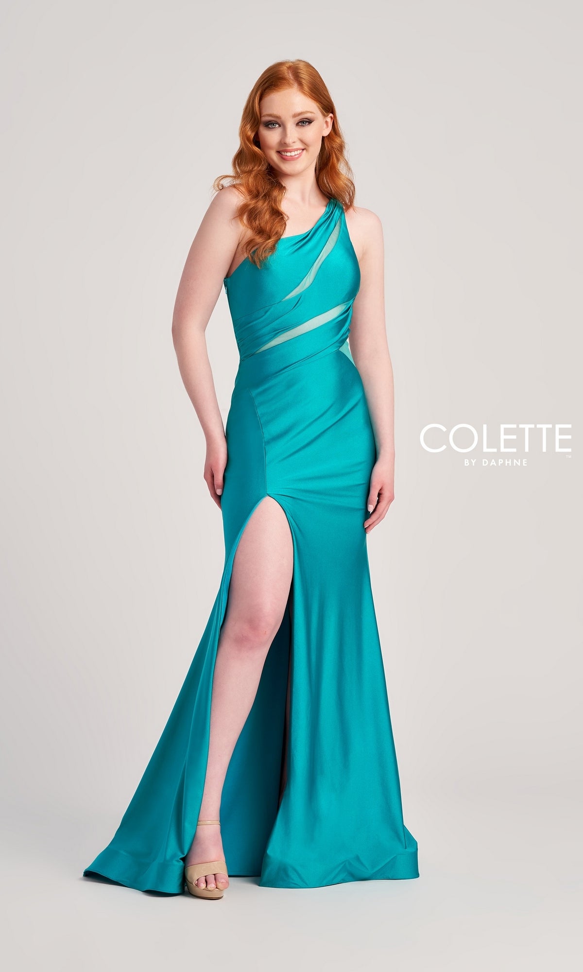 A woman poses before a plain background in the One-Shoulder Cut-Out Long Colette Prom Dress CL5207, featuring a teal hue, thigh-high slit, and visible Colette by Daphne logo, highlighting this stunning designer evening gown.